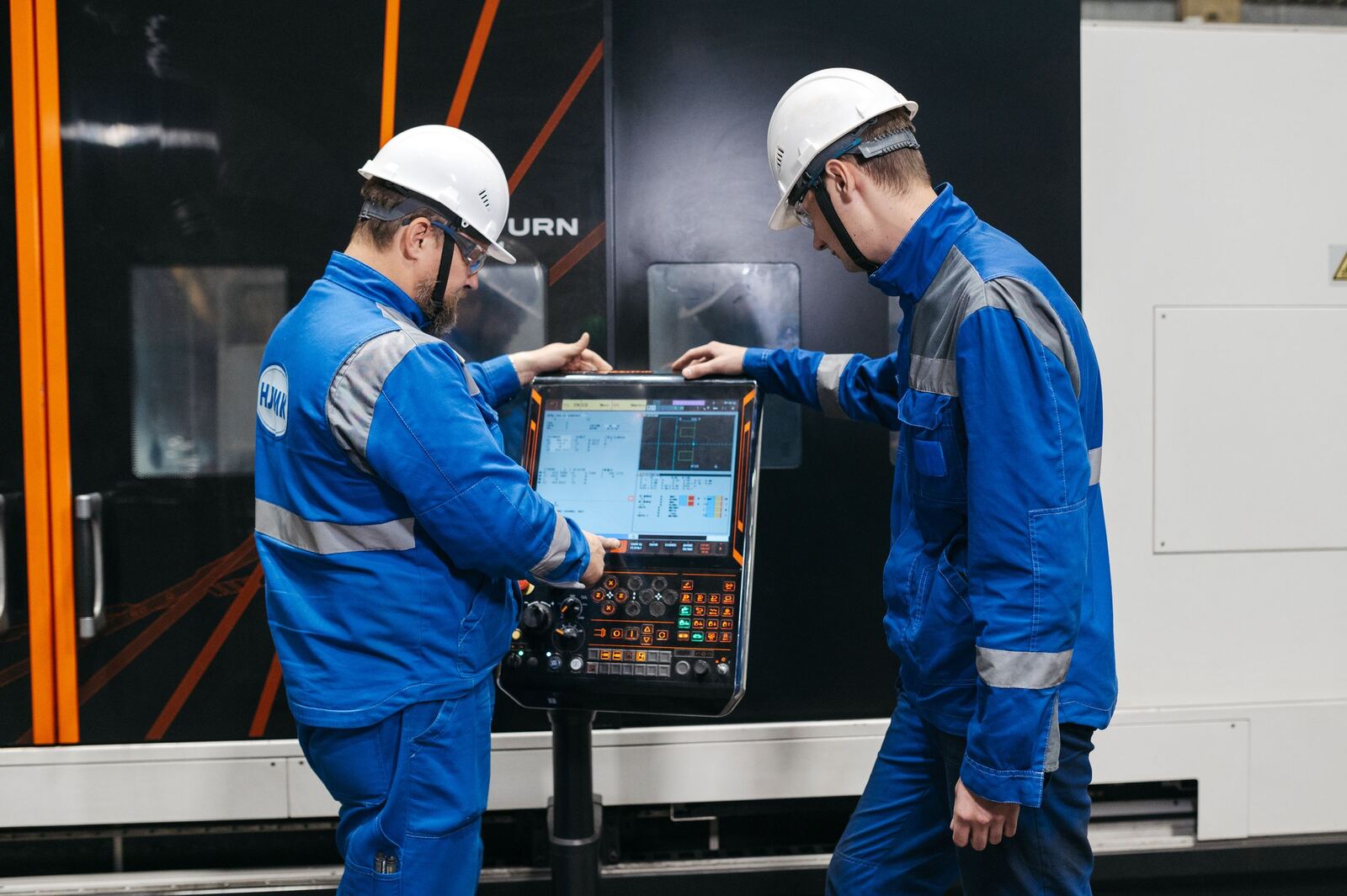 Two technicians in hard hats working at the control panel of a CNC machine